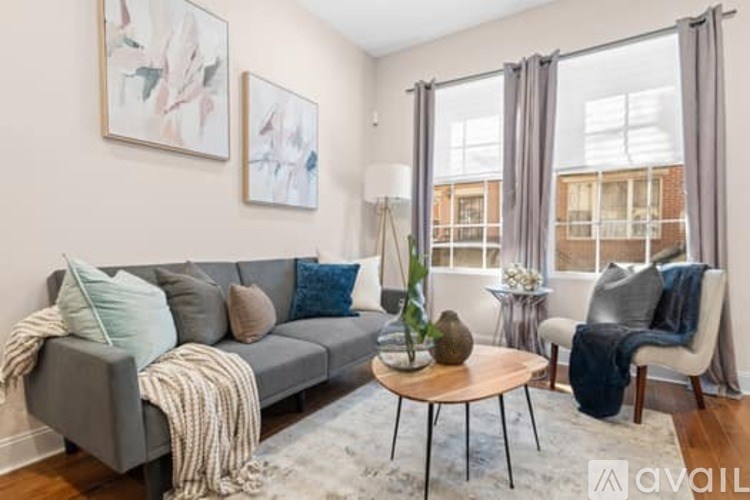 A living room with a grey couch, a wooden coffee table, and a large window with curtains.
