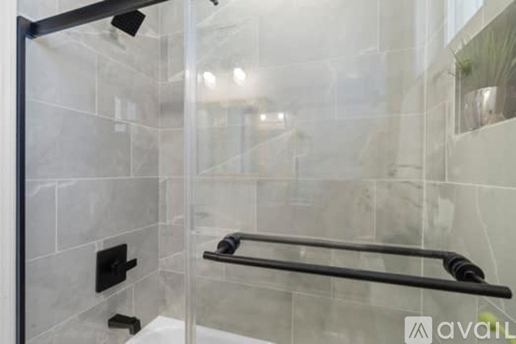 A modern bathroom with a glass shower door and a black grab bar.
