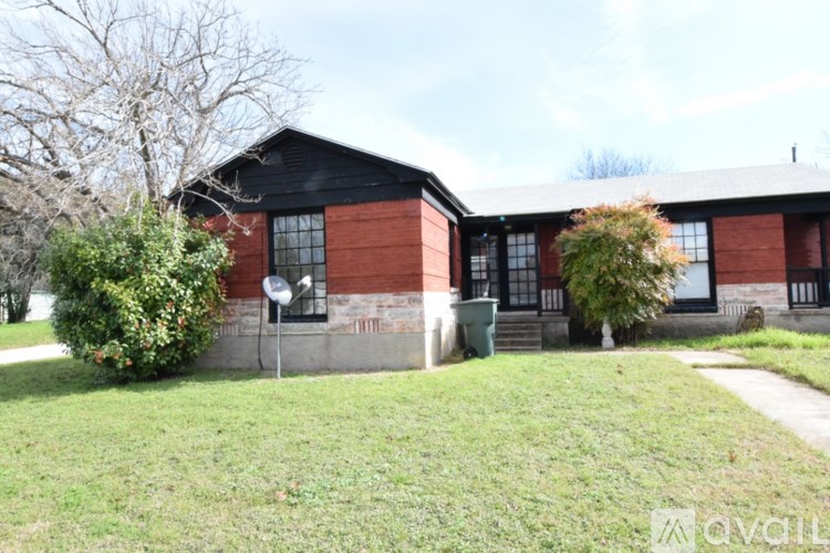 A red brick house with a black roof and a green trash can in front.