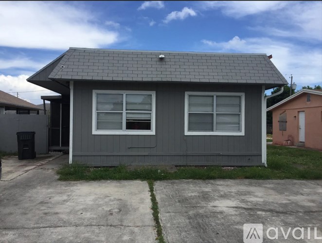 A grey house with a black trash can in front of it.