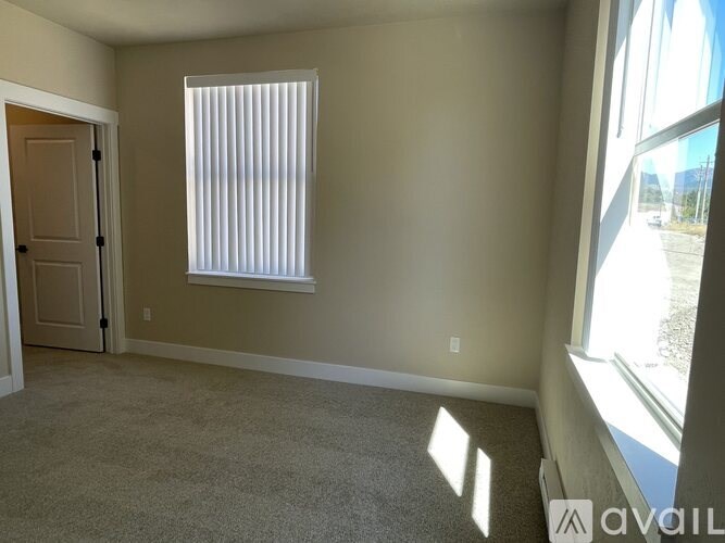 A room with a carpeted floor, a window with blinds, and a door leading to another room.