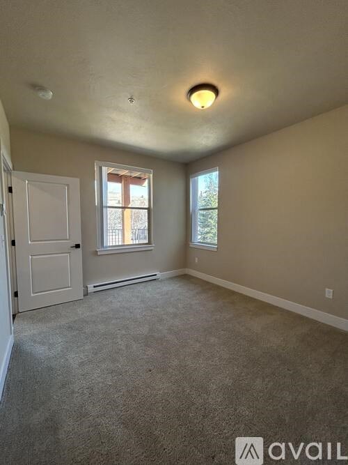 A room with a carpeted floor, a window with a view of trees, and a door.