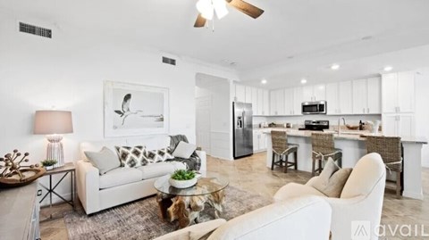 A modern living room with a white sofa set and a kitchen in the background.
