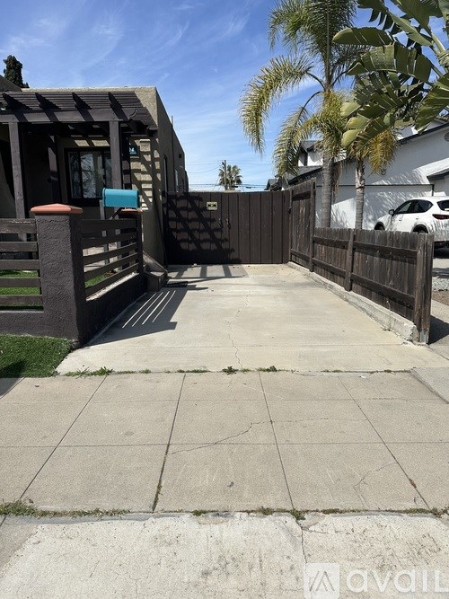 A concrete walkway leads to a wooden gate and a small building.
