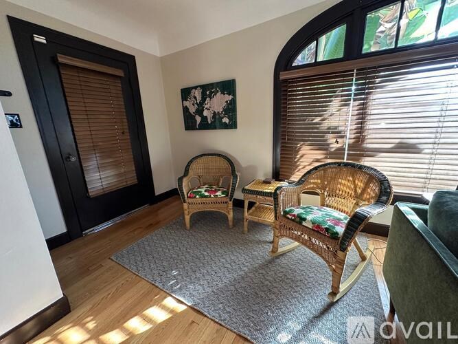 A room with a wicker chair and a grey rug.