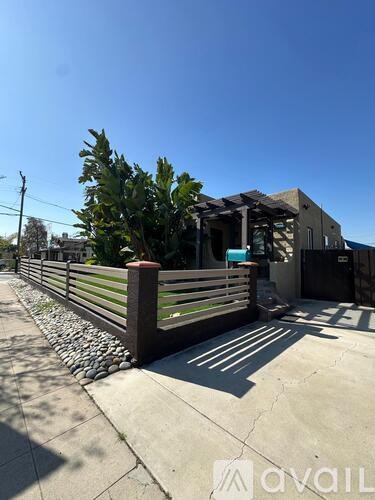 A sunny day on a sidewalk with a wooden fence and a building in the background.