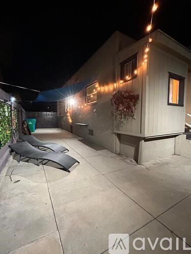 A patio area with a table and chairs is illuminated by string lights.