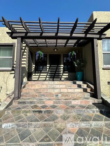 A house entrance with a wooden pergola and steps made of bricks.