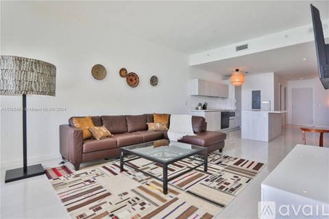 A living room with a brown couch, a glass coffee table, and a rug with a pattern.