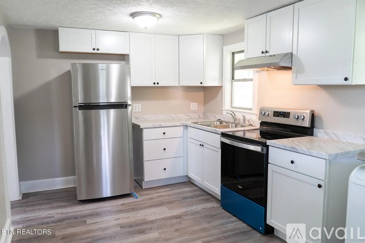 A kitchen with a stainless steel refrigerator, white cabinets, and a wooden floor.