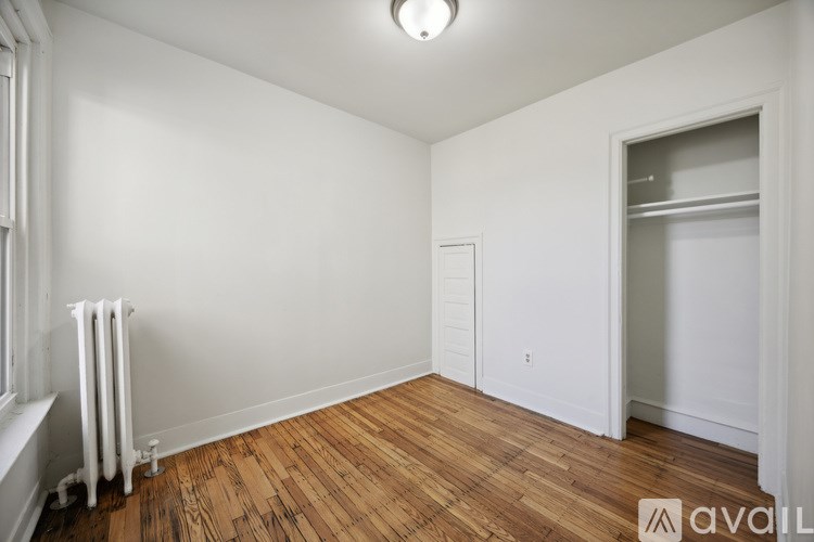 A room with wooden floors and white walls, with a window on the left and a door on the right.