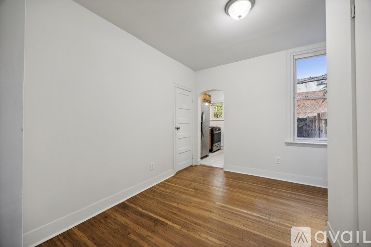 A room with wooden floors and white walls, with a door and a window.