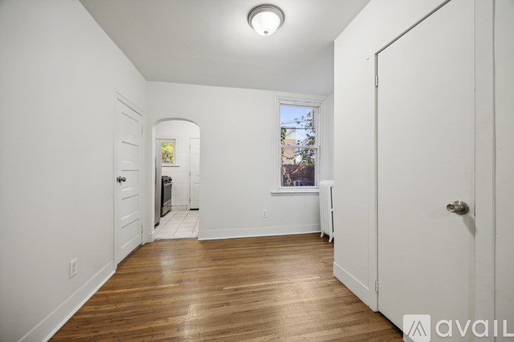 A room with white walls and wooden floors, with a window showing a view of buildings outside.