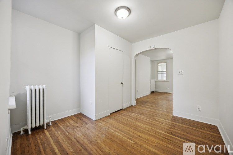 A room with wooden floors and white walls, with a radiator on the left side.
