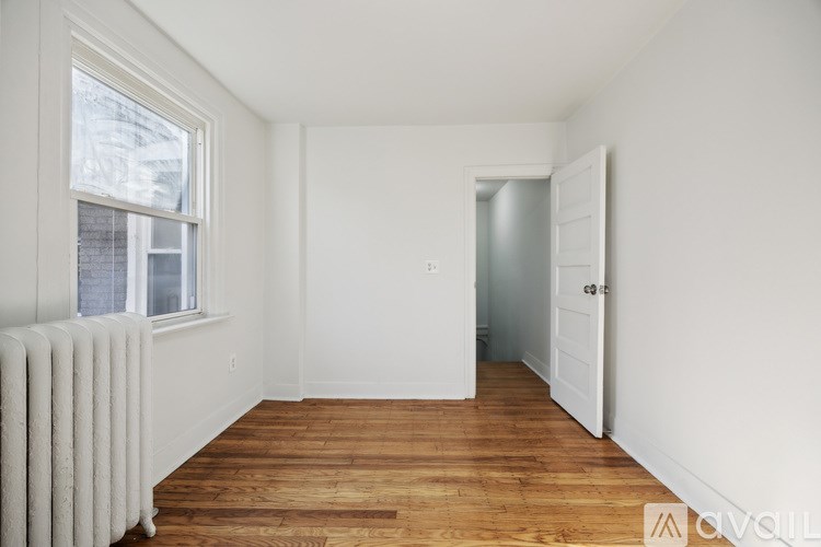 A room with wooden floors and white walls, with a window and a door.