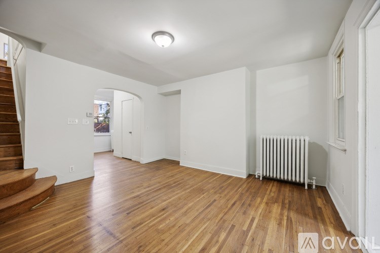 A spacious room with wooden floors and a staircase on the left side.