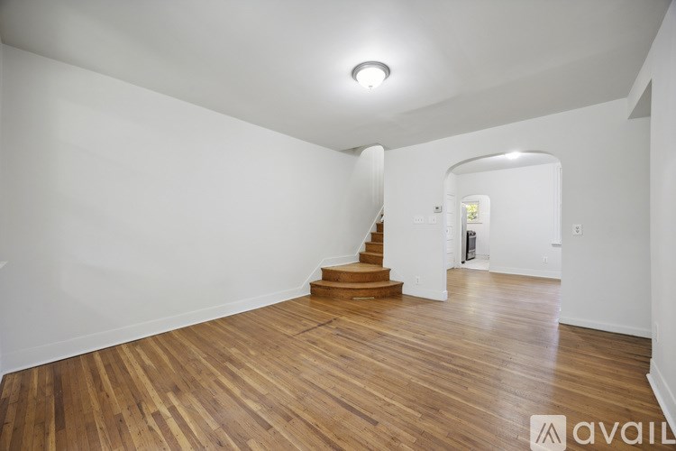 A spacious room with wooden floors and a staircase leading to another room.