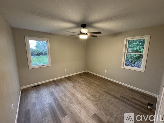A room with a ceiling fan and two windows.