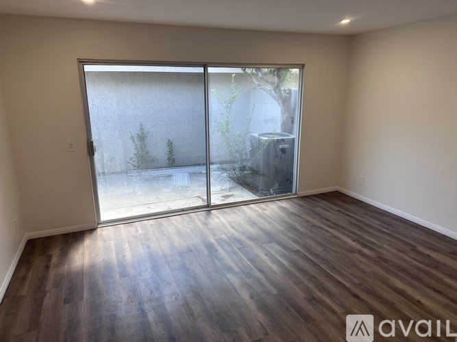 A room with wooden flooring and a sliding glass door leading to a backyard.