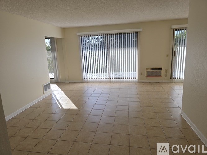 A spacious room with tiled flooring and a large window with blinds.