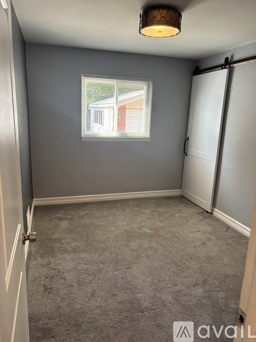 A room with grey carpet and a window showing a house outside.