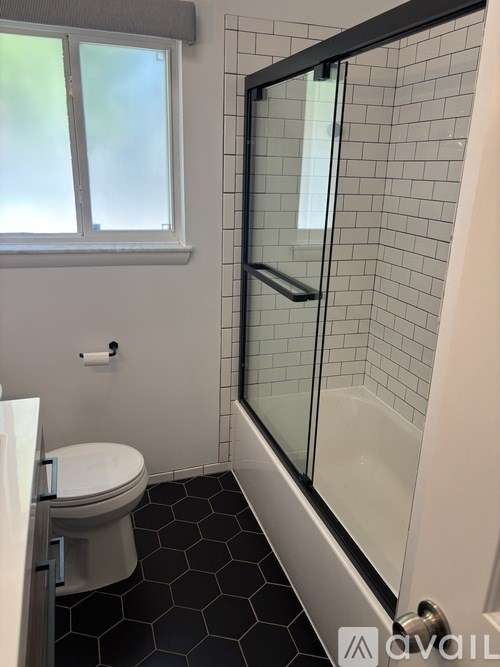 A bathroom with a toilet, a shower with a glass door, and a window.