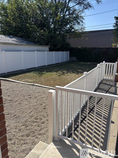 A white fence in a backyard with a brick wall on the left.