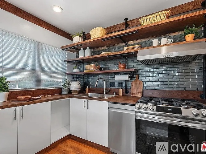 A kitchen with white cabinets and a wooden shelf above the stove.