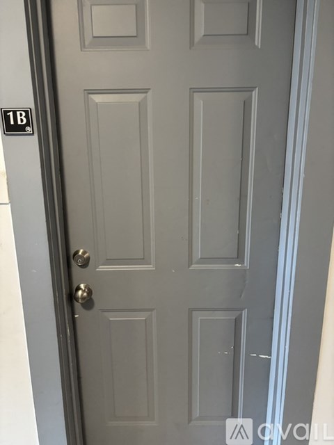 A grey door with a brass handle and a sign above it that says 1B.