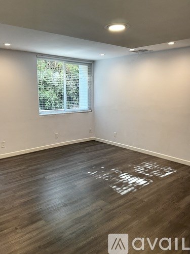 A room with wooden flooring and a window with a view of trees outside.