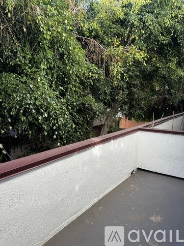 A balcony with a white wall and a red border with trees in the background.