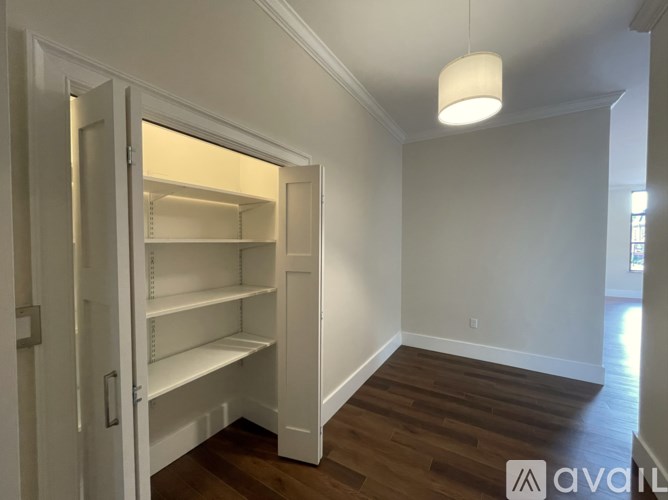 A white pantry with an open door and a light hanging from the ceiling.