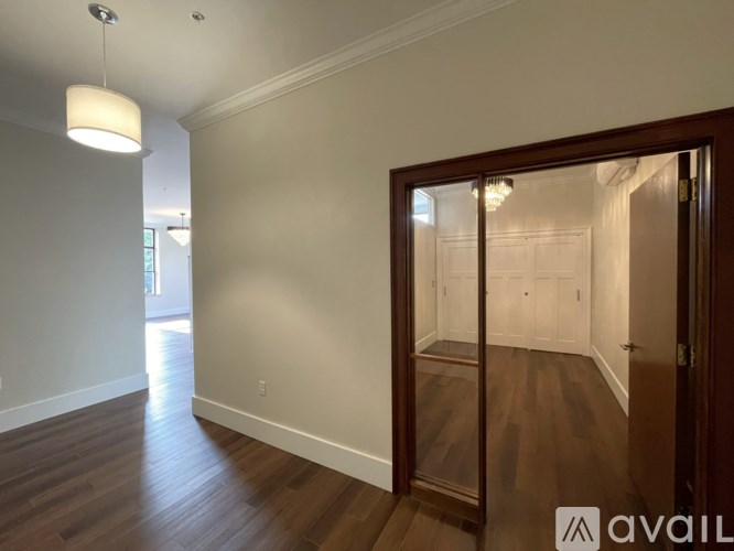 A room with wooden floors and a white wall with a door leading to another room.