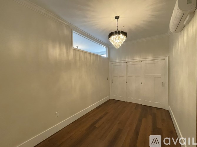 A room with wooden floors and white walls, featuring a chandelier and a window.