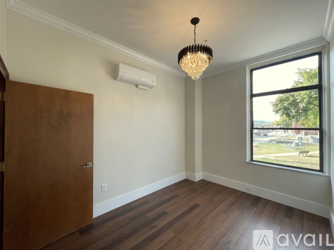 A room with a wooden floor, a brown door, a chandelier, and a window showing an outdoor scene.