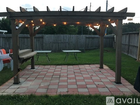 A wooden pergola with string lights is over a patio with a picnic table and chairs.