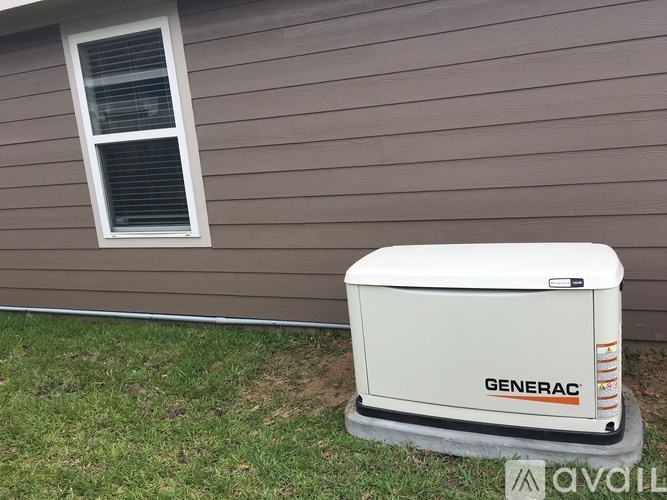 A white Generac generator sits on a concrete slab in front of a house.