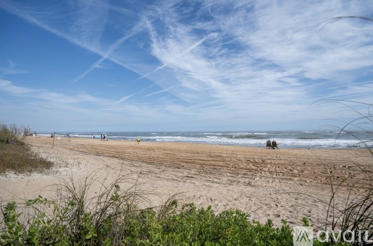 A beach scene with people walking on the sand and the ocean in the distance.