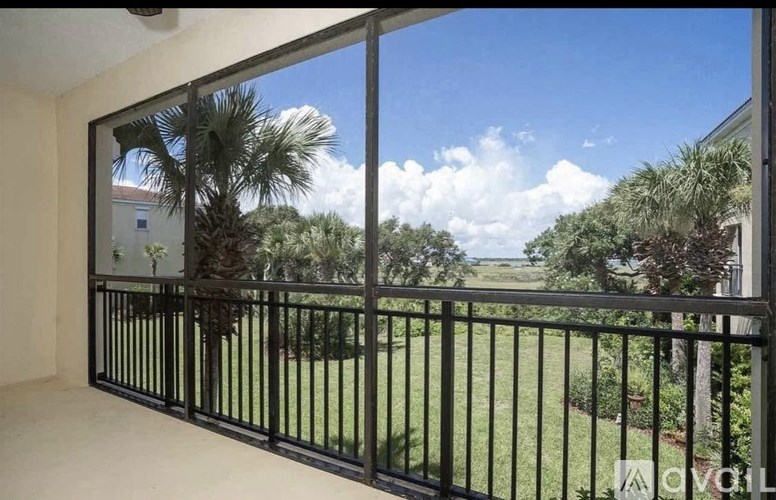 A balcony with a black railing overlooks a green lawn and trees.