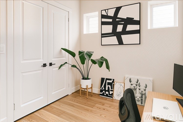 A room with a plant, a laptop, and some pictures on the wall.