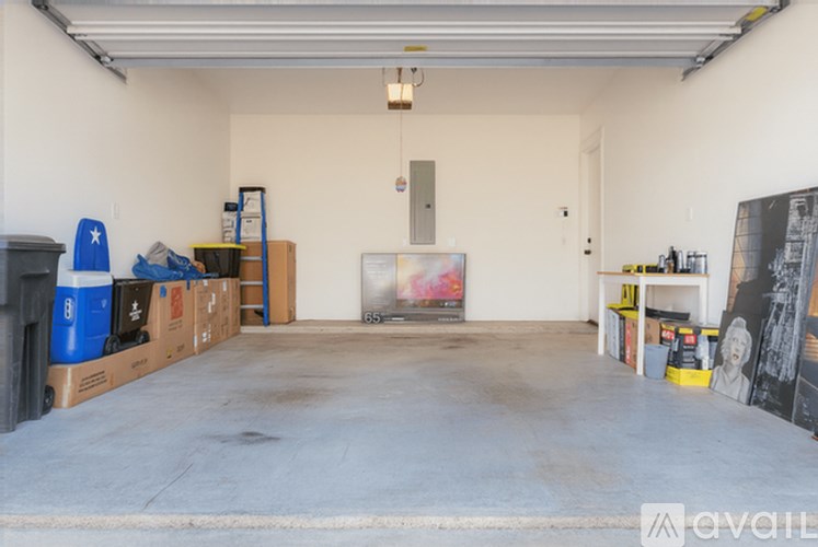 A spacious garage with a concrete floor and white walls, containing various items such as cardboard boxes, a ladder, and a painting.