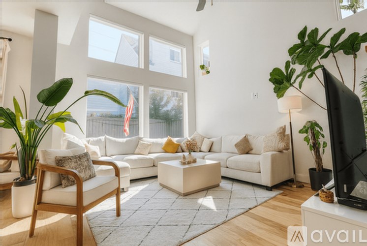 A living room with a white couch, a wooden chair, a white coffee table, a flat screen TV, and a potted plant.