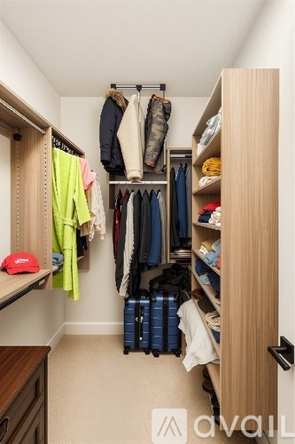A small closet with clothes hanging and a suitcase on the floor.
