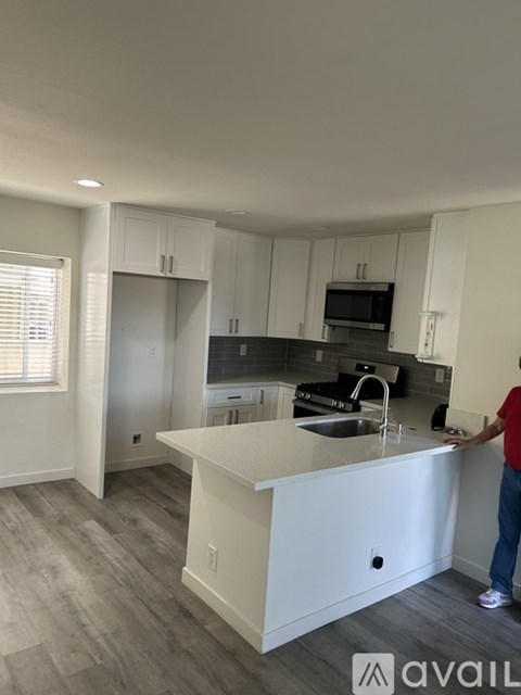 A person stands in a kitchen with white cabinets and a large island.