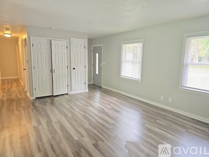 A room with wood flooring and white walls has a window with blinds and a door.