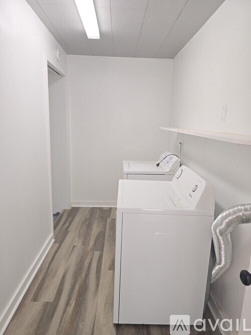 A white washing machine is in a small room with a wood floor and a wall.