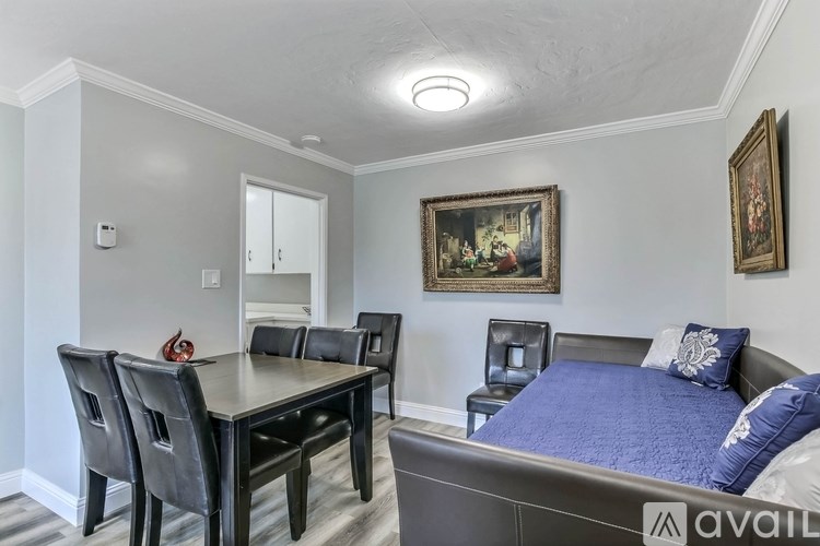 A bedroom with a bed, a dining table and chairs, and two framed paintings on the wall.