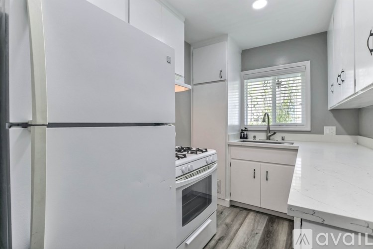 A white refrigerator stands in a kitchen with a stove and sink.