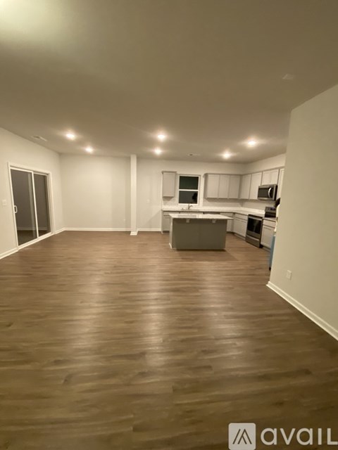 A spacious room with wooden flooring and a kitchen area in the background.
