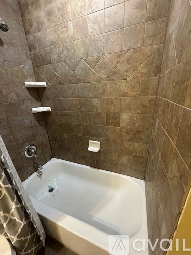 A bathroom with a white bathtub and brown tiled walls.